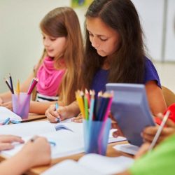 Two Female Students Coloring At Table While Smiling