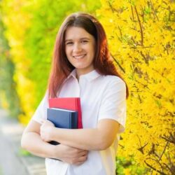 Aws Girl Wearing White Blouse Smiling With Textbooks Infront Of Yellow Flowers