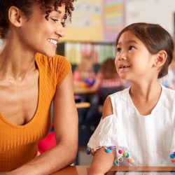 Young Girl Student Smiling Up At Female Teacher