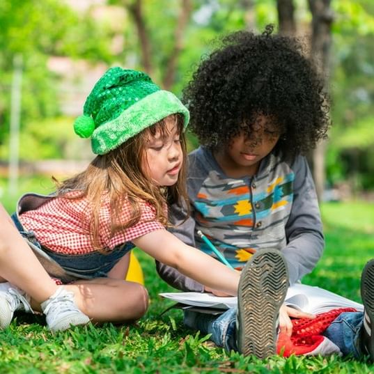 Boy And Girl Student Sitting In Grass Doing Homework