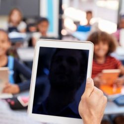 Teacher Holding Tablet In Front Of Class