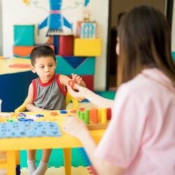 Small Student Reaching For Block From Female Teacher S Hand