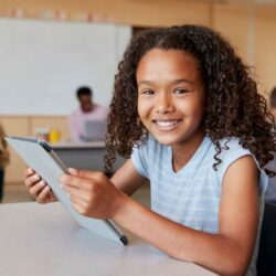 Female Student Of Color Holding Tablet And Smiling