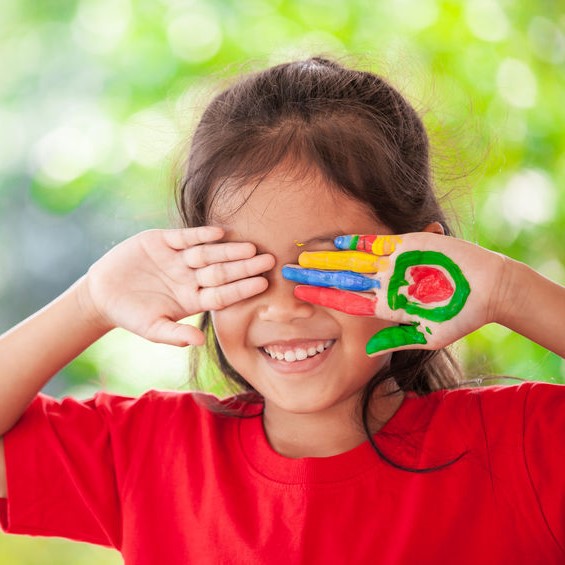 Little Girl Smiling While Covering Her Eyes With Paint On Her Palms