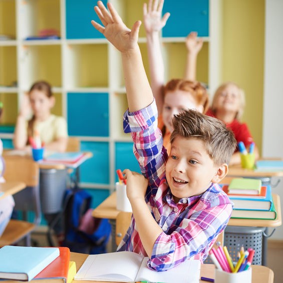 Happy Kids Raising Their Hands While Sitting At School Desks